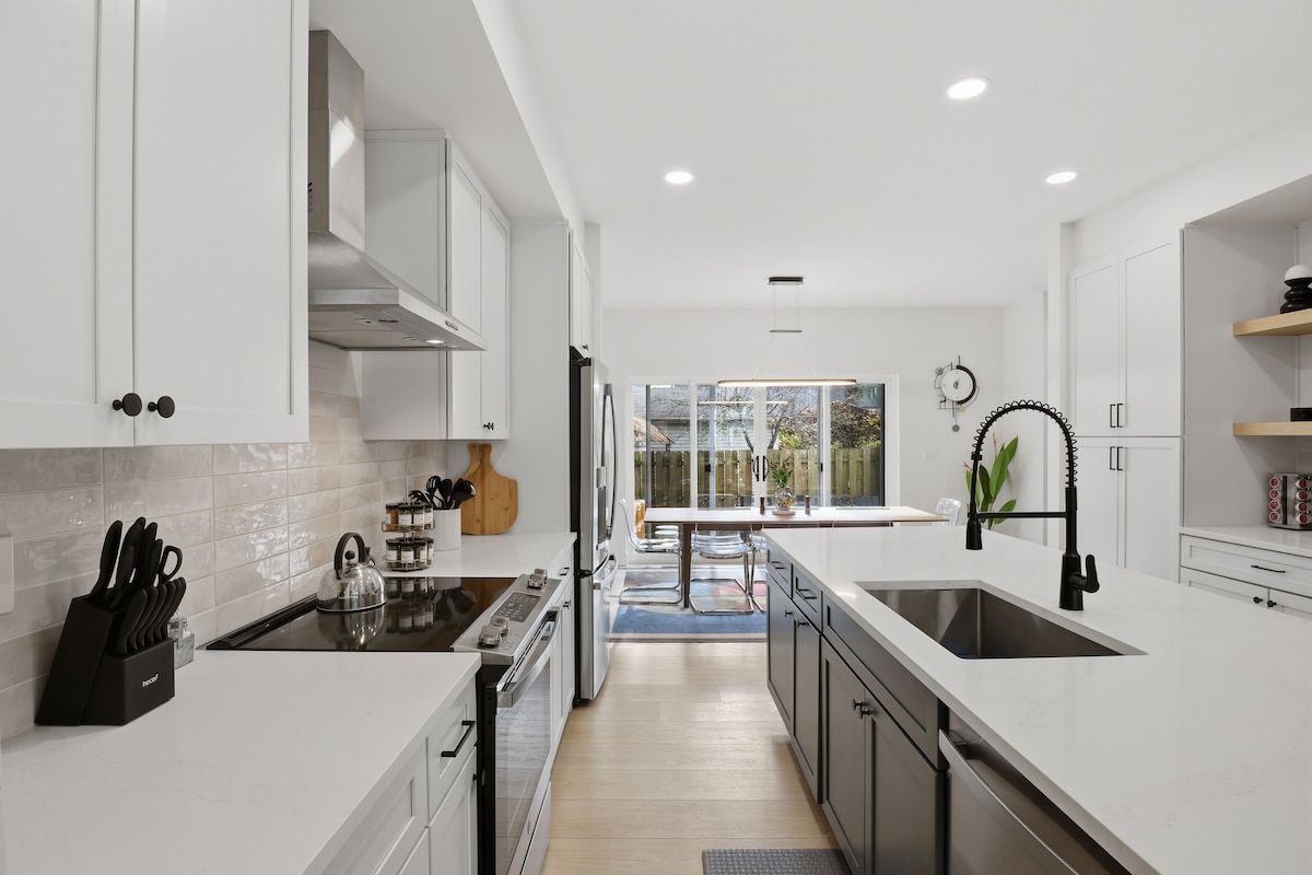 A modern kitchen with white cabinetry, a central island, and a view to the outside.