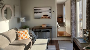 A modern living room with a sofa, a coffee table, a dining table, and a view of the outside. - Harbourview Galley - with Patio/ Air Conditioning/ Steps to Downtown/ 1 Bedroom (St. John's)