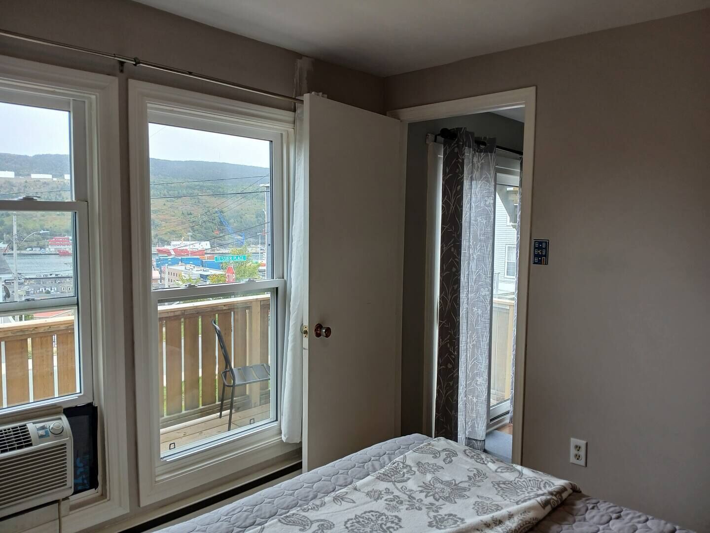 Et soveværelse med en seng, et vindue med udsigt over bybilledet og en dør, der fører til en balkon.