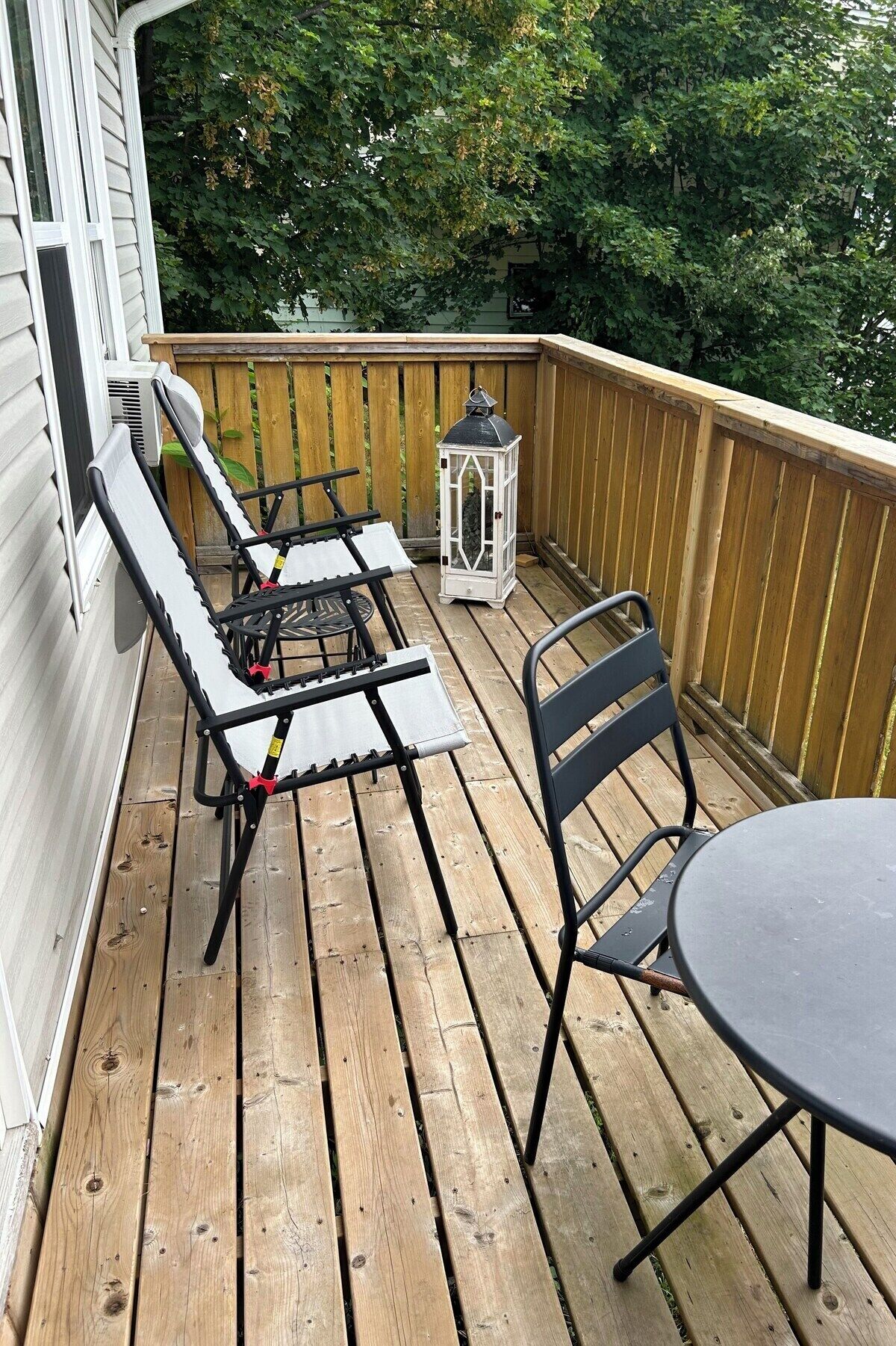 A wooden deck with a table and two chairs, a lantern, and a window.