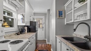 A narrow kitchen with white cabinets, a granite countertop, a stainless steel sink, and a black refrigerator. - Harbourview Galley - with Patio/ Air Conditioning/ Steps to Downtown/ 1 Bedroom (St. John's)