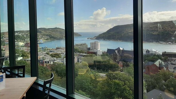 A view from a high-rise window overlooking a coastal town with a harbor, buildings, and hills. - Harbourview Galley - with Patio/ Air Conditioning/ Steps to Downtown/ 1 Bedroom (St. John's)