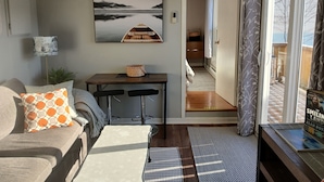 A living room with a sofa, a coffee table, a dining table with two chairs, a painting on the wall, and a view through an open door. - Harbourview Galley - with Patio/ Air Conditioning/ Steps to Downtown/ 1 Bedroom (St. John's)