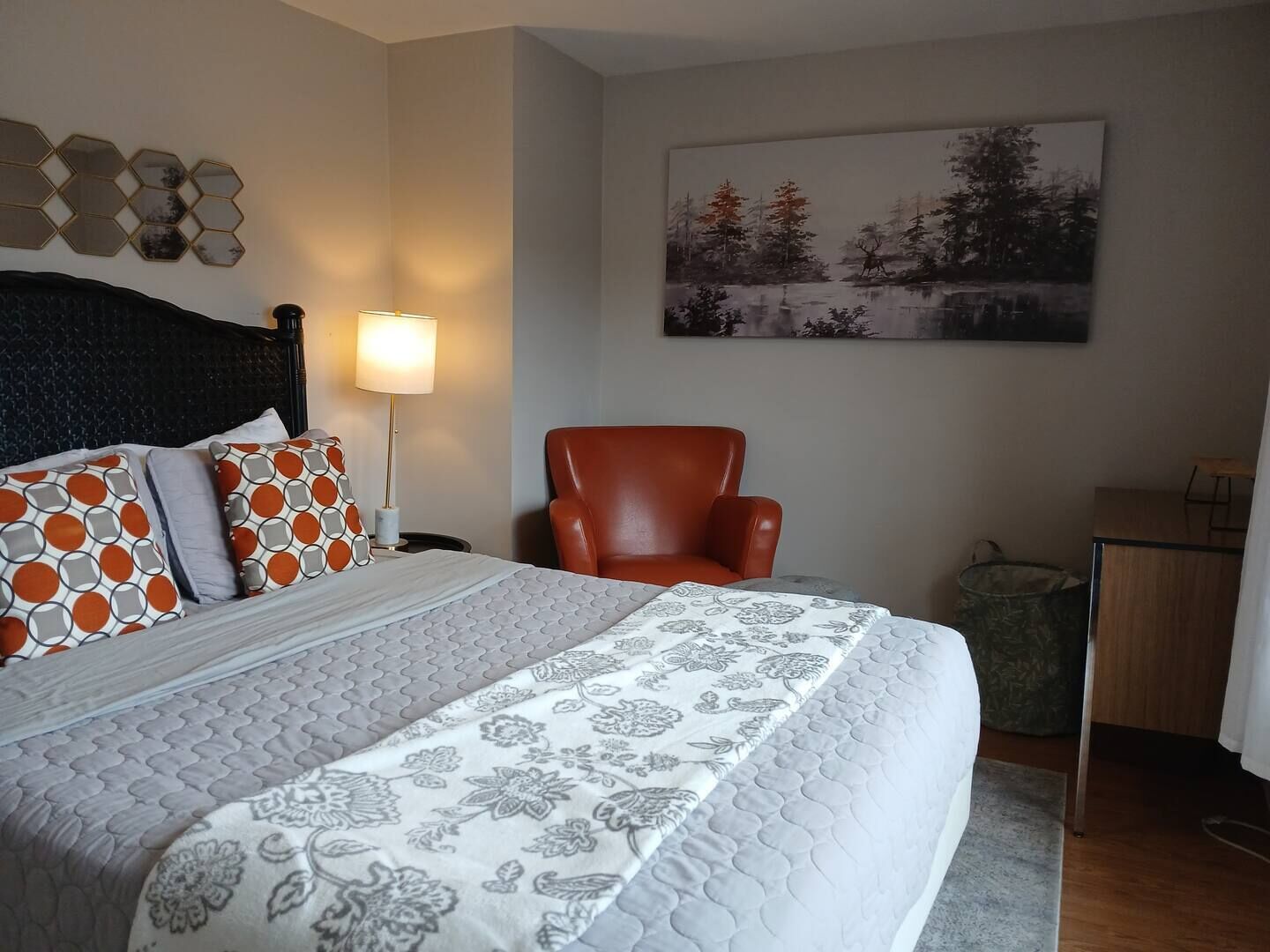 Une chambre à coucher avec un lit, une chaise, une lampe, un tableau et une petite table.