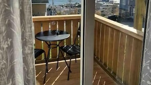 A balcony with a table and chairs, a view of a body of water, and buildings in the distance. - Harbourview Galley - with Patio/ Air Conditioning/ Steps to Downtown/ 1 Bedroom (St. John's)