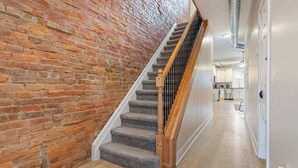 A staircase with a brick wall on one side and a wooden floor on the other, leading to a kitchen area. - East End Pittsburgh 4 Bedroom Getaway (Pittsburgh)