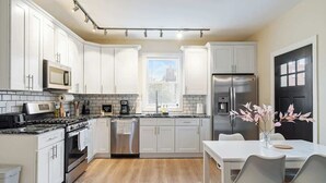A modern kitchen with white cabinets, stainless steel appliances, and a dining area with a white table and chairs. - East End Pittsburgh 4 Bedroom Getaway (Pittsburgh)