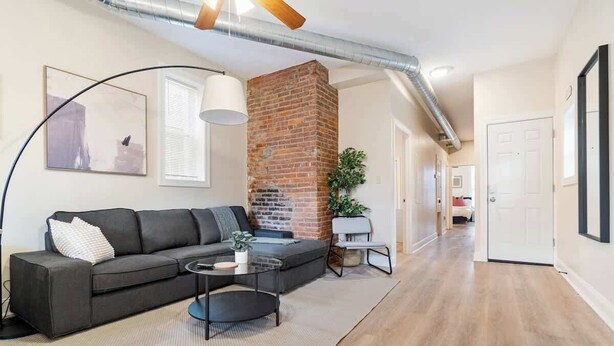 A modern living room with a brick fireplace, a sofa, a coffee table, and a potted plant. - East End Pittsburgh 4 Bedroom Getaway (Pittsburgh)
