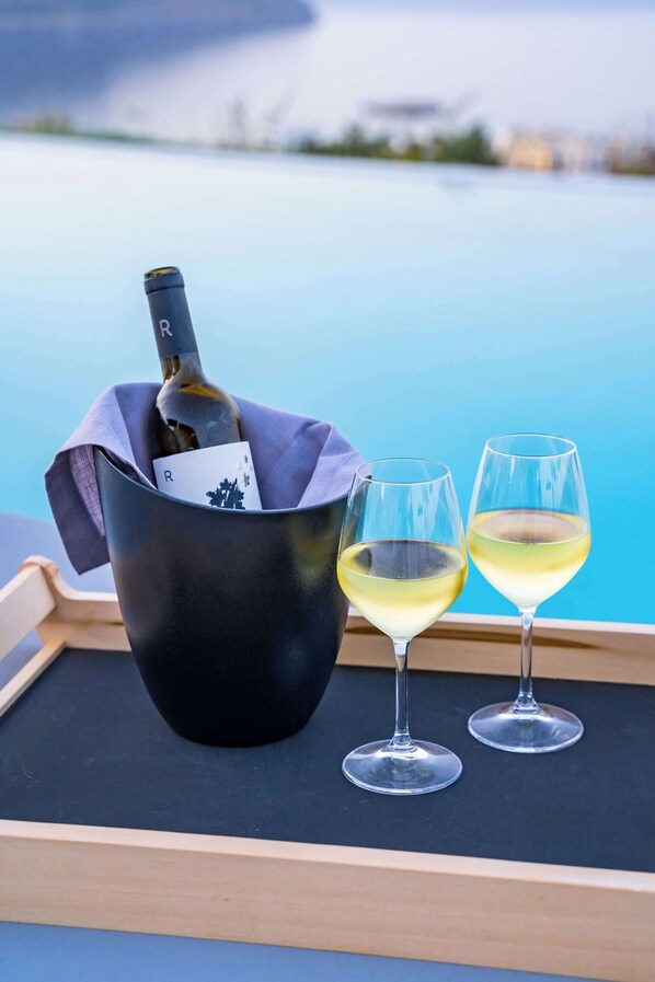 A black bucket with a bottle of wine and two glasses on a tray by a pool.