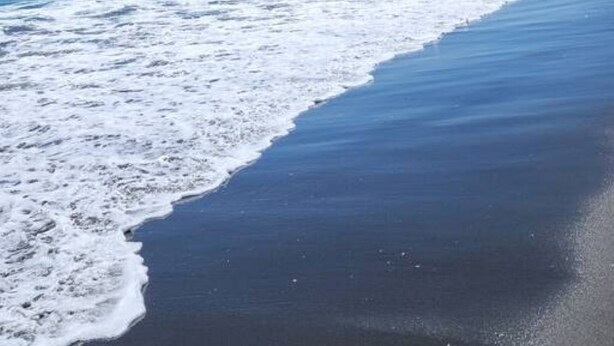 Ein Strand mit sanft anschwellenden Wellen unter blauem Himmel.