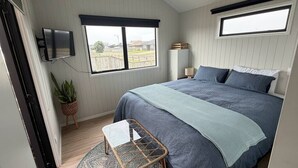 Ein Schlafzimmer mit Bett, Wandfernseher, Fenster, Nachttisch und einer Topfpflanze.