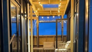 Eine Holzterrasse mit Glasverkleidung, einer Bank und Blick auf das Wasser.