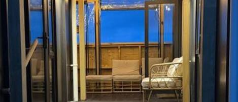 A wooden deck with a glass enclosure, a bench, and a view of the water.