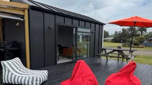 Eine moderne Außenterrasse mit Holzboden, Glastür und Picknicktisch mit rotem Sonnenschirm.