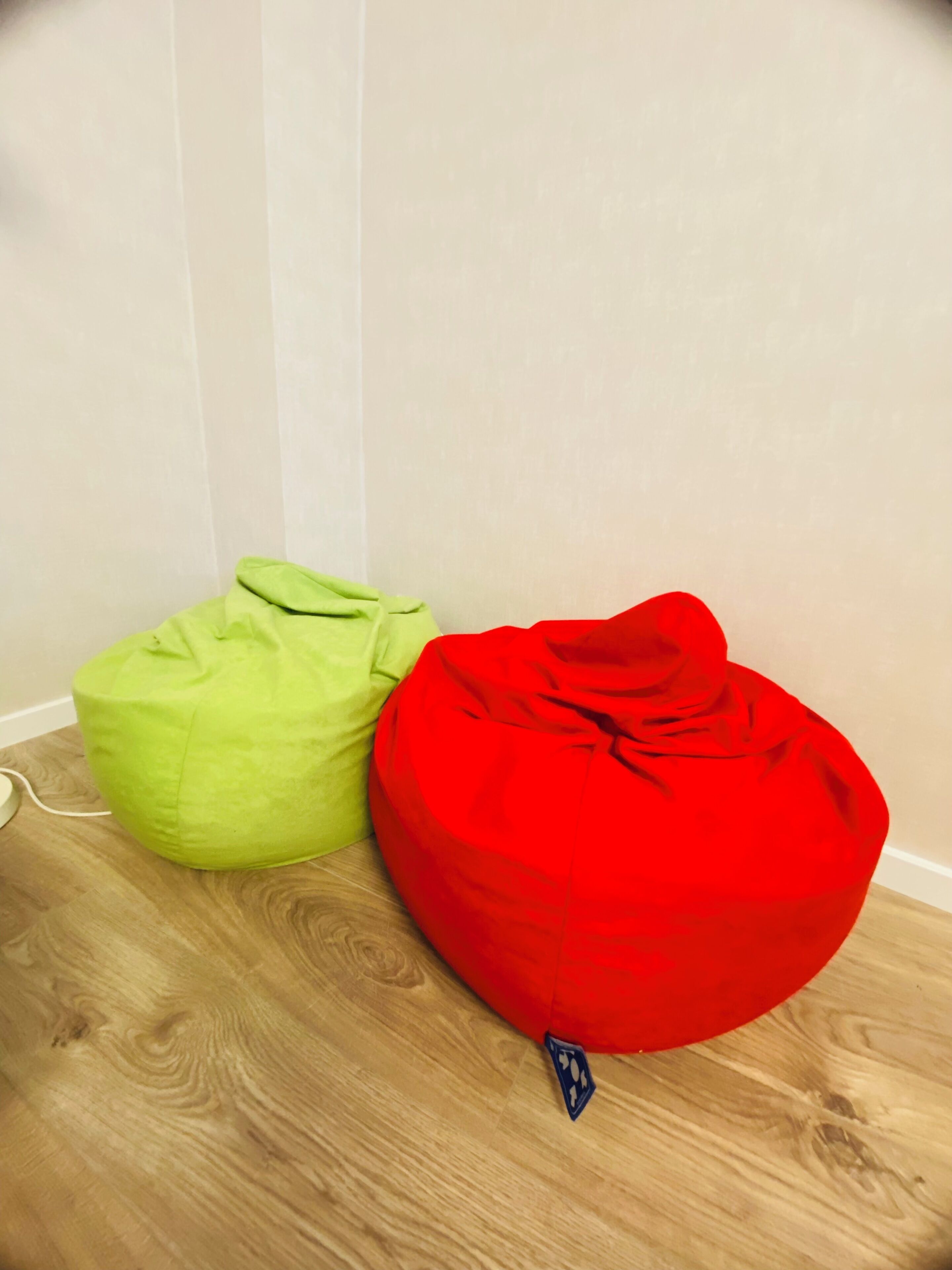 Zwei Sitzsäcke, ein grüner und ein roter, auf einem Holzboden vor einer Wand platziert.