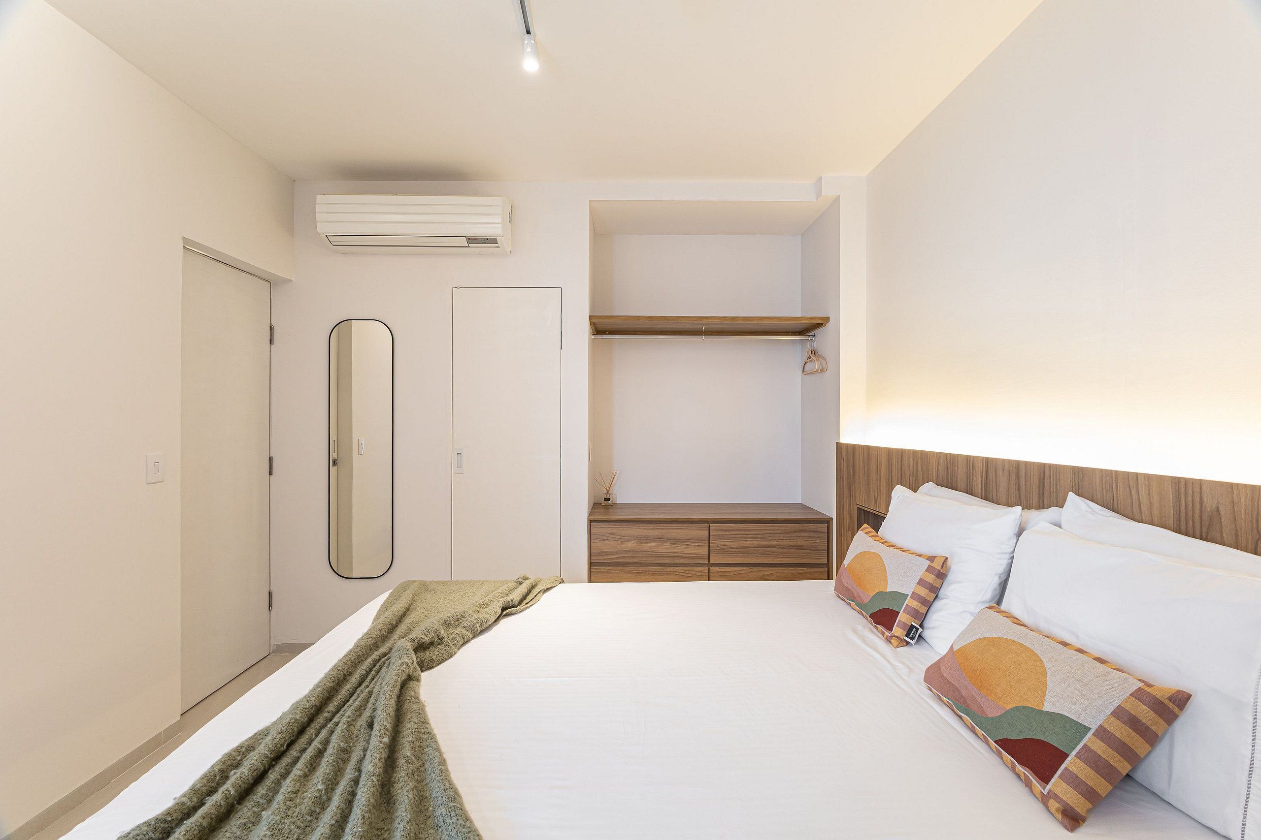 Un dormitorio con cama, mesita de noche, espejo, armario y estante empotrado.