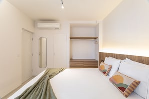 Un dormitorio con cama, mesita de noche, espejo, armario y estante empotrado.