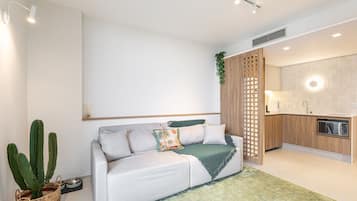 A modern living room with a sofa, a cactus plant, and a kitchen area with wooden cabinets and a microwave.