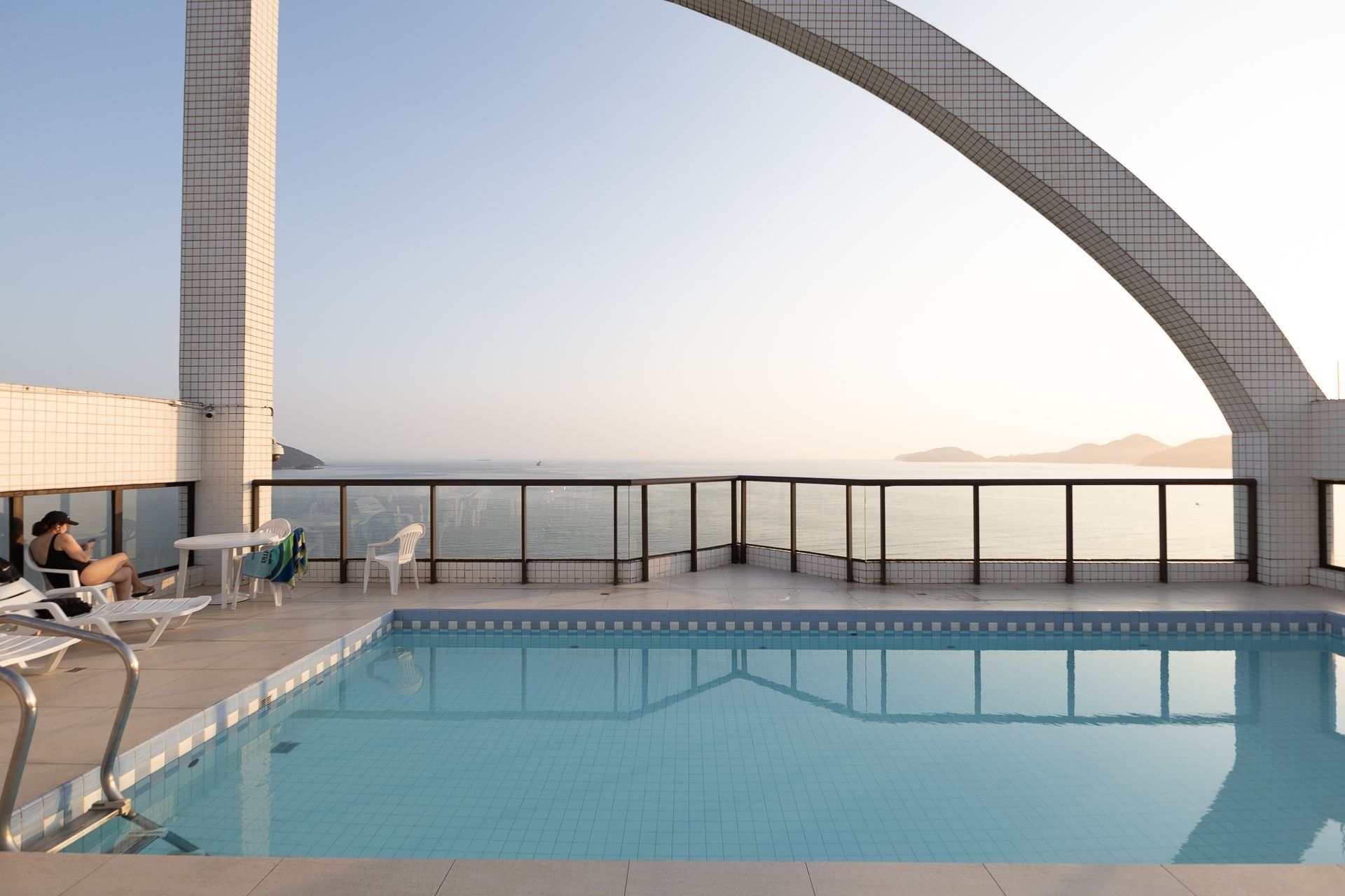 A rooftop pool with a clear view of the sea, a tiled deck, and lounge chairs.
