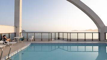 A rooftop pool with a clear view of the sea, a tiled deck, and lounge chairs.