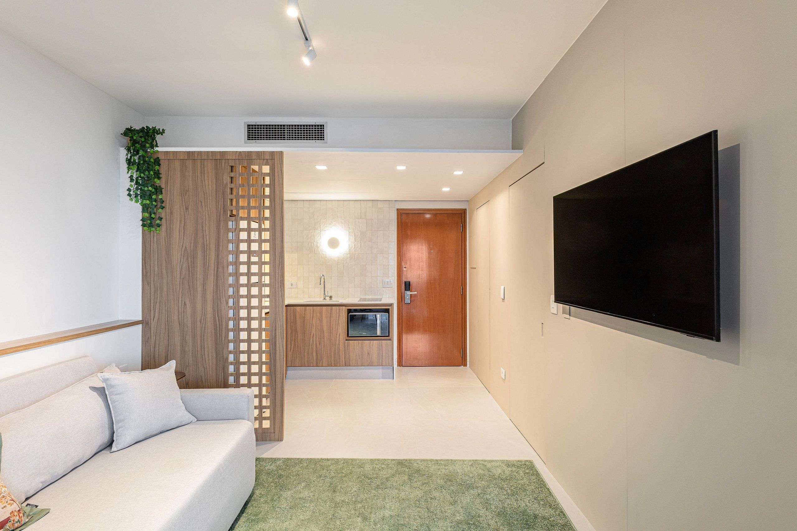 A modern living room with a sofa, a TV mounted on the wall, and a kitchen area in the background.