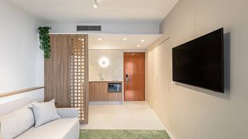 A modern living room with a sofa, a TV mounted on the wall, and a kitchen area in the background.