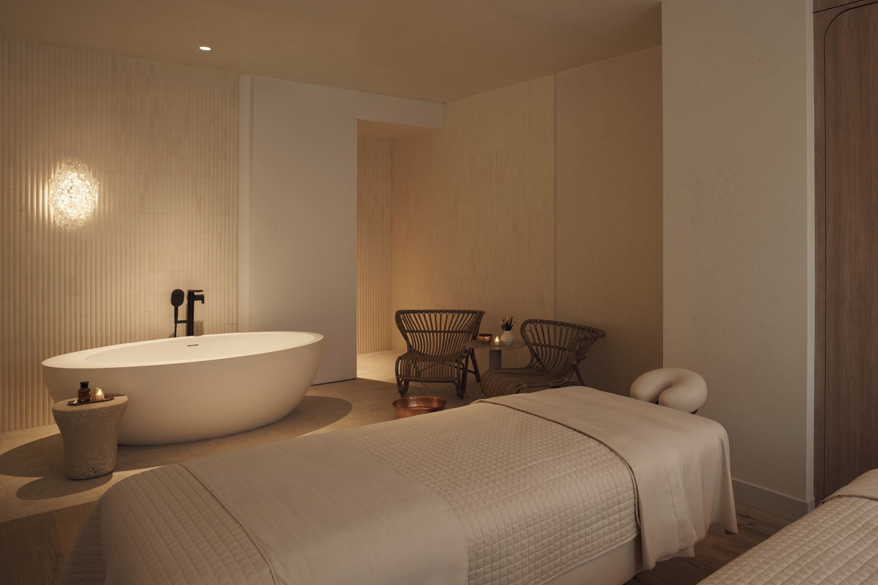 Une salle de bain moderne avec une baignoire sur pieds, deux fauteuils en osier, une petite table avec des bougies et une table de massage.