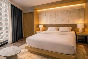 A modern hotel room with a large bed, two bedside tables with lamps, a marble side table, and a decorative wall panel.