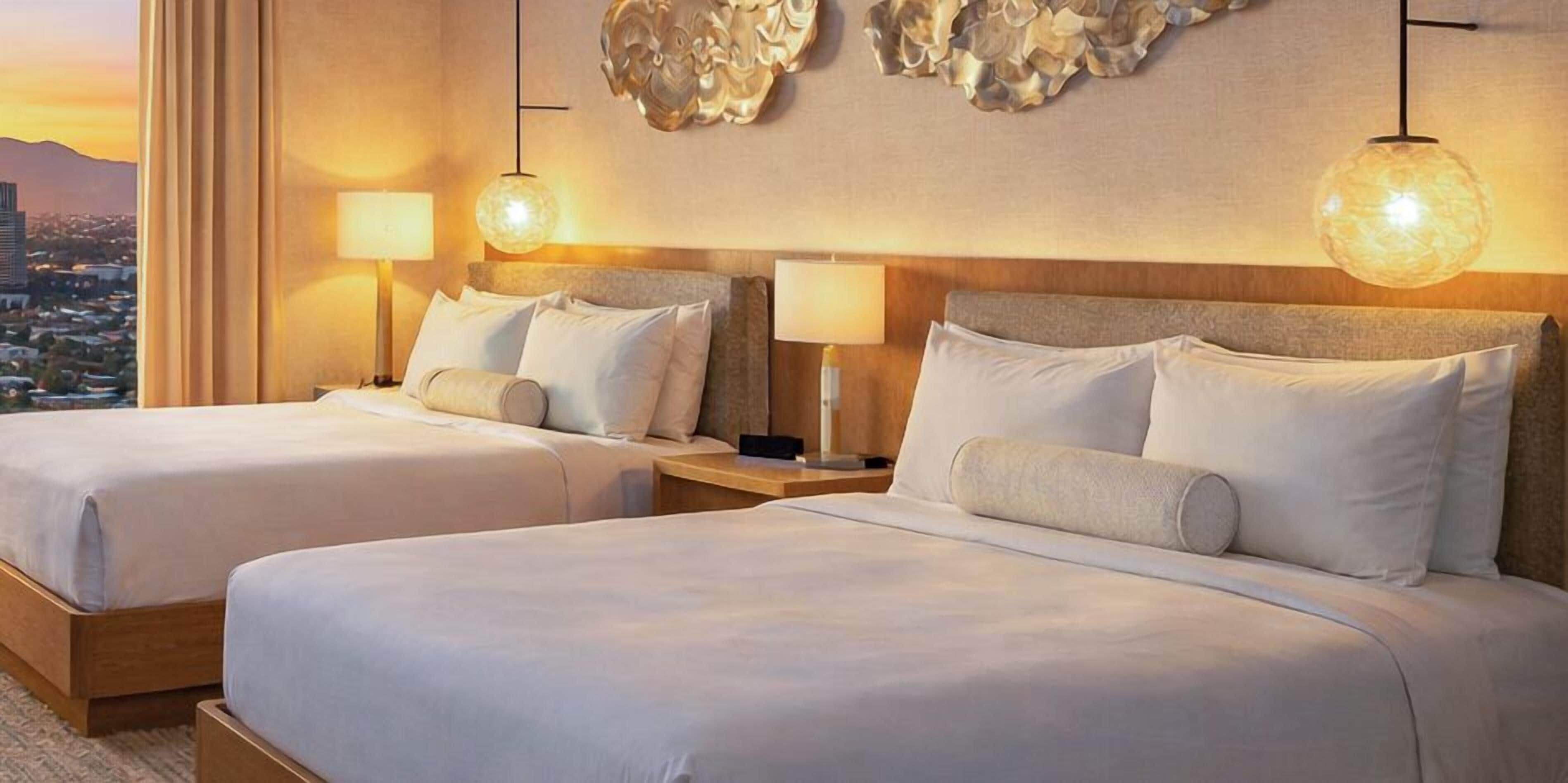 A hotel room with two beds, nightstands, lamps, and a city view.