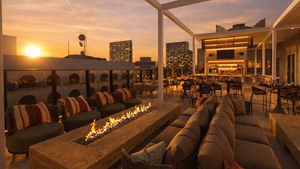 A rooftop bar with a fire feature, seating, and a city skyline view. - Denu Hotel & Spa (Phoenix)
