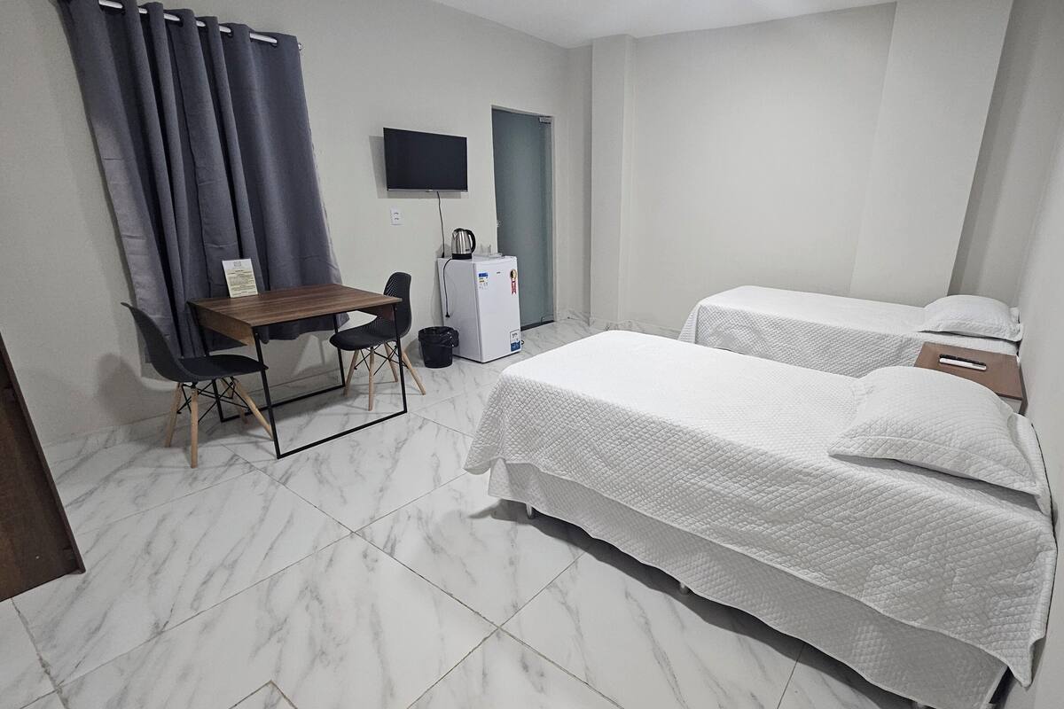 A hotel room with two beds, a desk, a chair, a television, and a refrigerator.