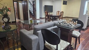 A living room with a glass coffee table, grey sofas, a chess table, and a staircase.
