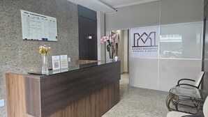 A reception desk with a schedule board, a QR code for payment, and a sign for Mendes Residence Studios & Suites.