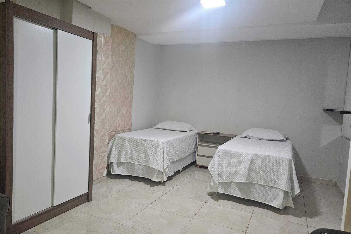 A small, clean room with two single beds, a wardrobe, and a bedside table.