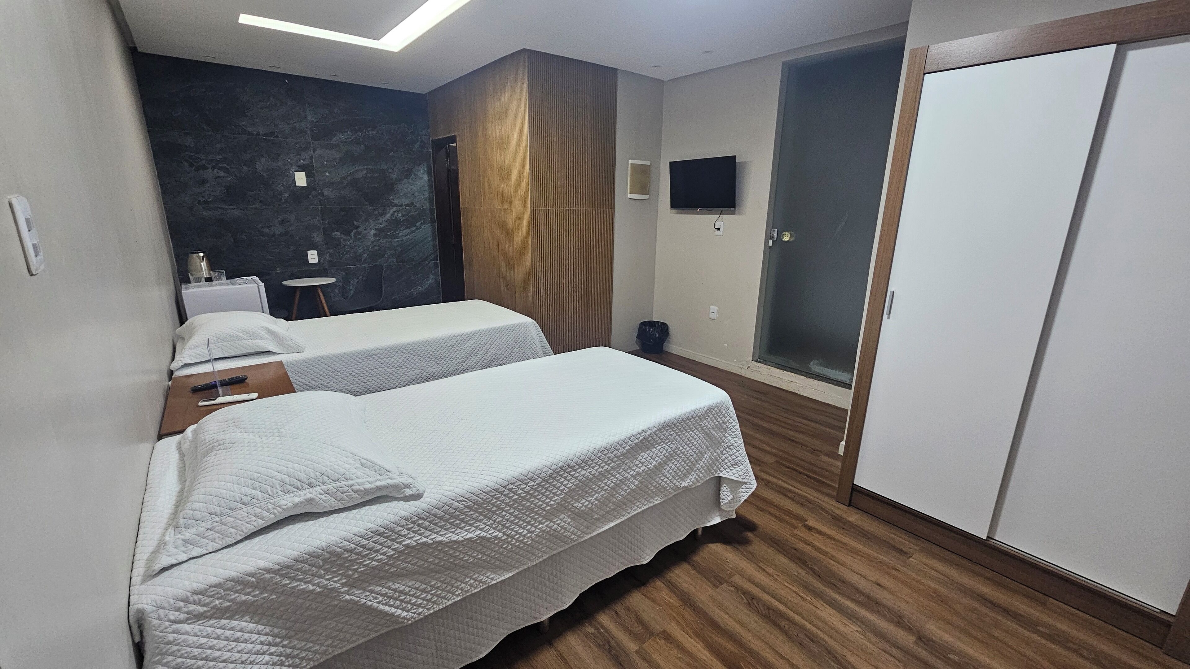 A hotel room with two beds, a wooden floor, a dark wall, a TV, and a wardrobe.