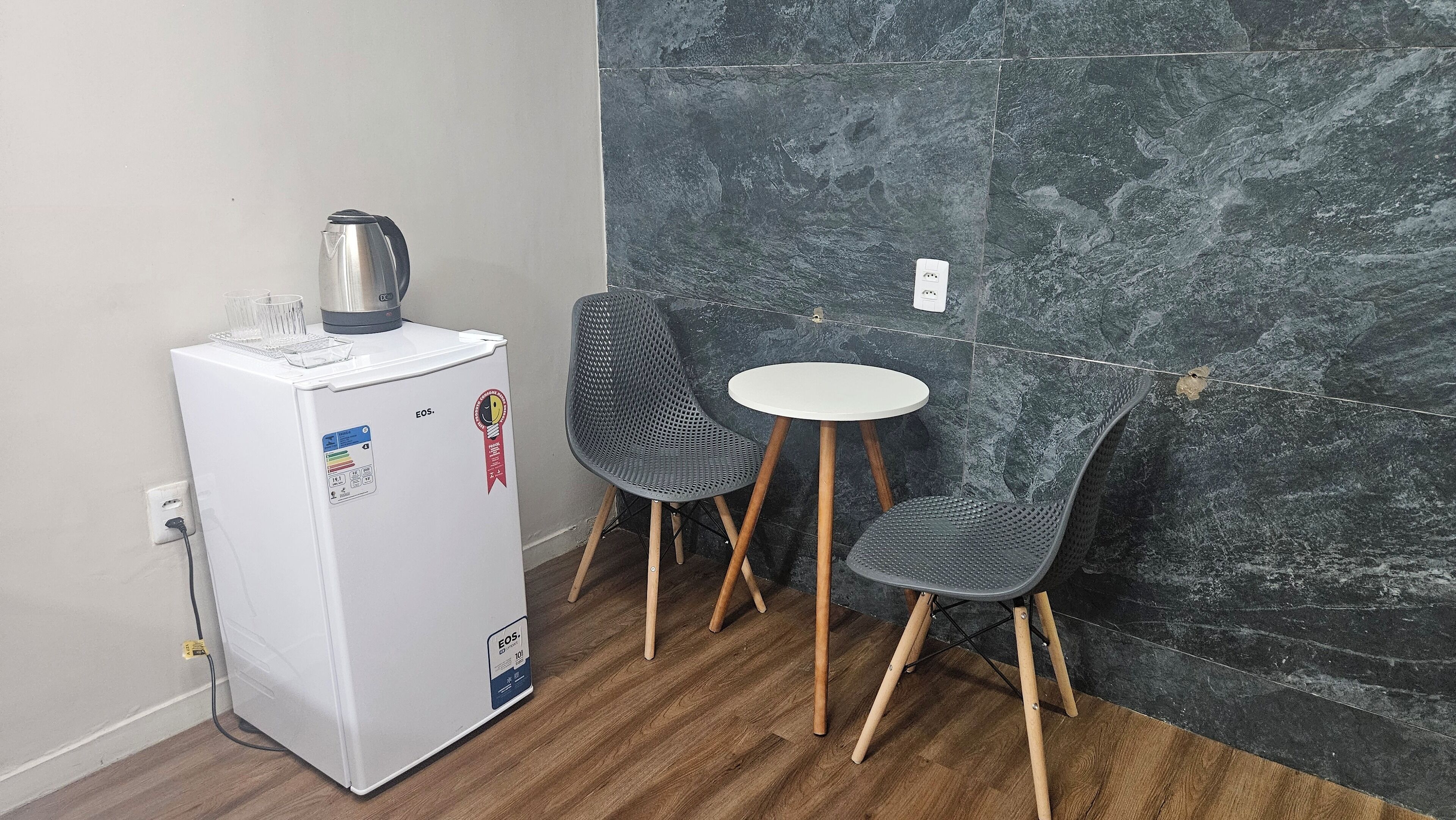 A compact kitchenette with a refrigerator, a kettle, and a small table with two chairs.