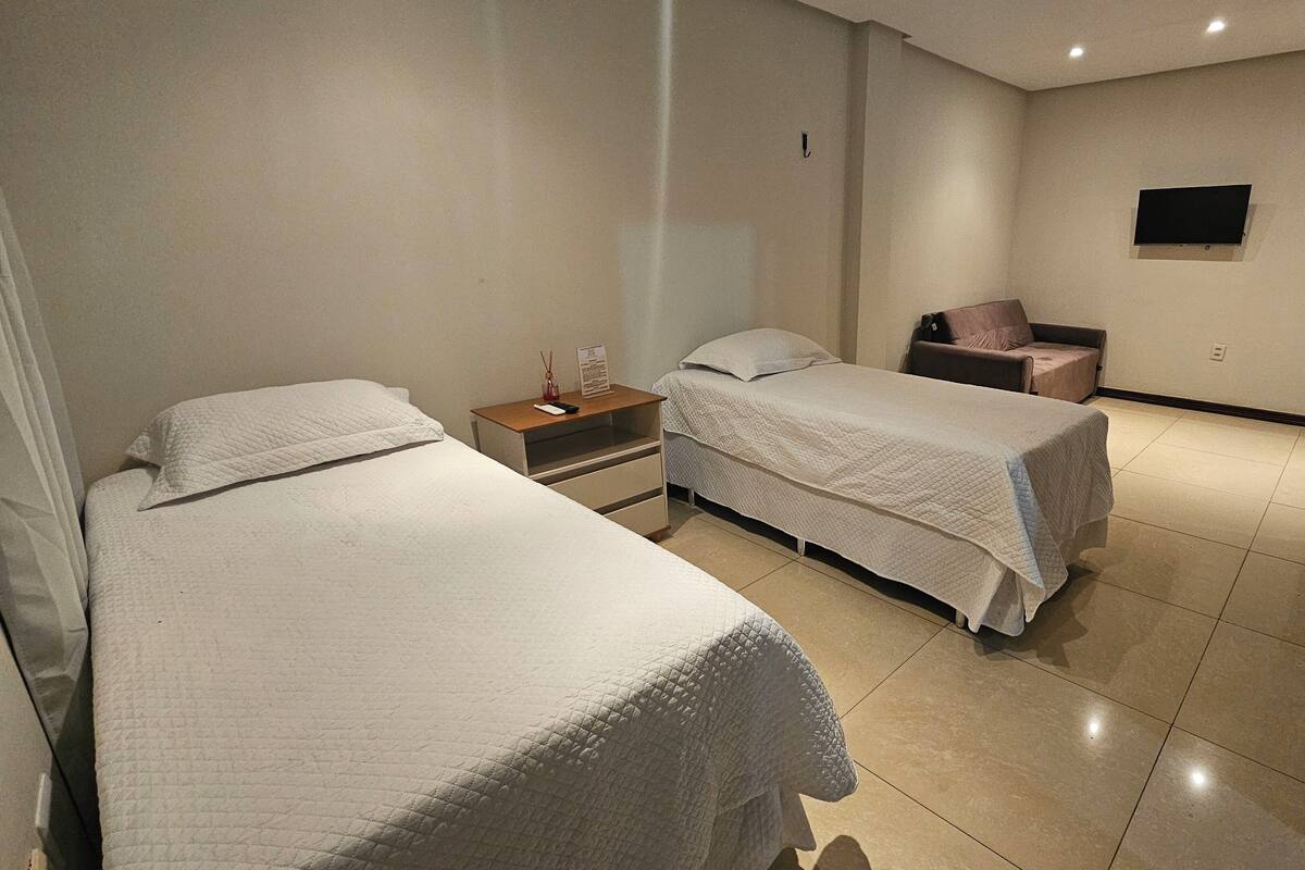 A hotel room with two beds, a nightstand, a chair, and a TV mounted on the wall.
