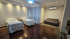 Une chambre d’hôtel avec deux lits simples, un canapé, une petite table et un appareil de climatisation.