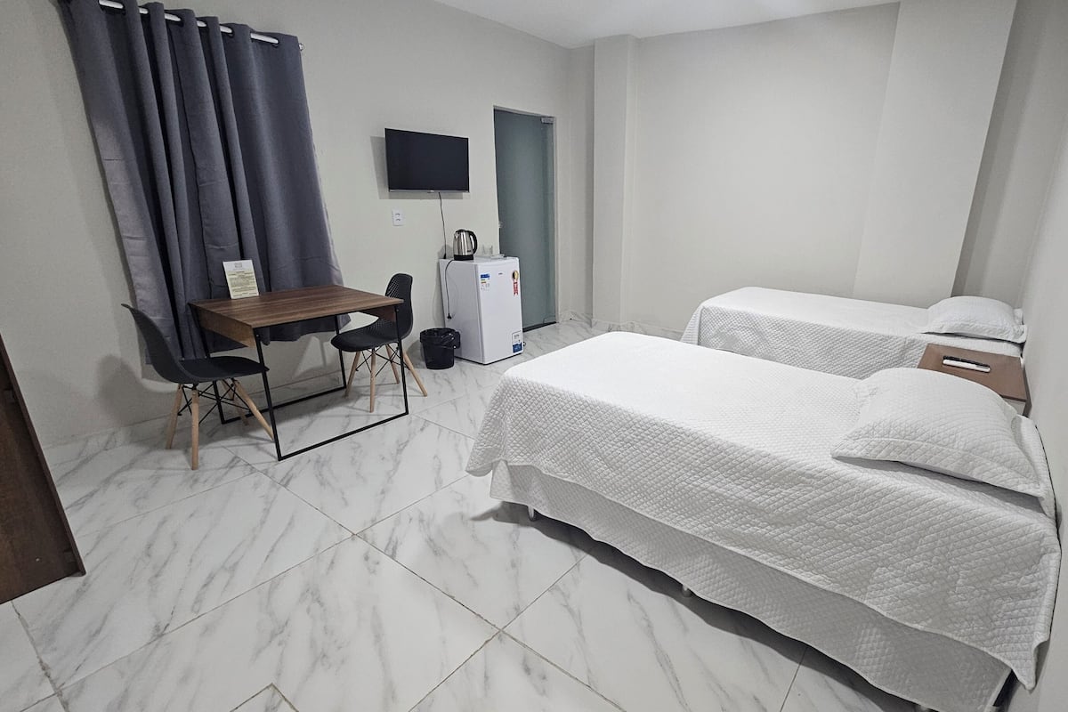 A hotel room with a bed, a desk, a chair, a TV, and a refrigerator.