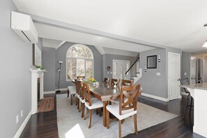 A dining area with a long table, chairs, a fireplace, and a staircase leading to another room.