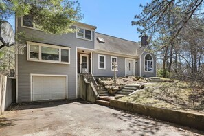 A two-story house with a garage, a staircase leading to the second floor, and a yard with a stone retaining wall.