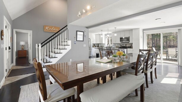 A spacious dining area with a wooden table, cushioned chairs, and a bench. A staircase leads to an upper level. - Family-Friendly Mashpee Retreat w/ Outdoor Fun (Mashpee)