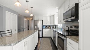 A modern kitchen with white cabinetry, stainless steel appliances, granite countertops, and pendant lighting. - Family-Friendly Mashpee Retreat w/ Outdoor Fun (Mashpee)