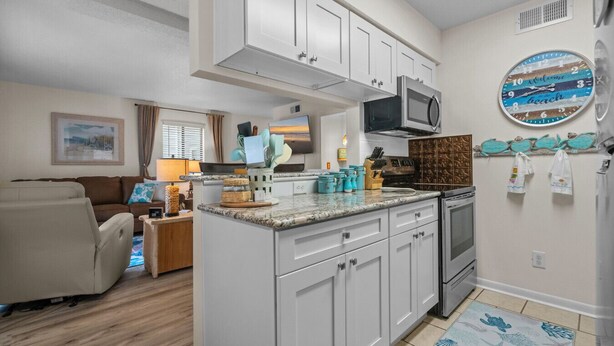Cocina compacta con armarios blancos, microondas y un reloj en la pared.