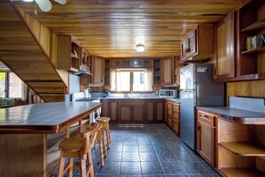 A kitchen with wooden cabinets, a central island with stools, a refrigerator, and a microwave. - Driftwood Gardens Guesthouse: Spacious, fully-equipped 2 bedroom Value Apartment (Placencia)