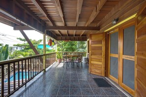 A wooden porch with a tiled floor, a table with chairs, and a view of a swimming pool. - Driftwood Gardens Guesthouse: Spacious, fully-equipped 2 bedroom Value Apartment (Placencia)