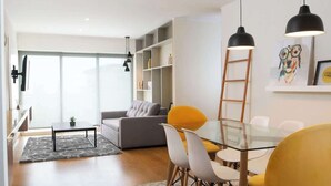 Una sala moderna con una mesa de comedor de vidrio, sillas amarillas, un sofá gris y una estantería.
