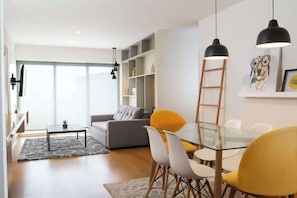 A modern living room with a glass dining table, yellow chairs, a grey sofa, and a bookshelf. - 2 APTS in One Building · Ideal for Large Groups! (Miraflores)