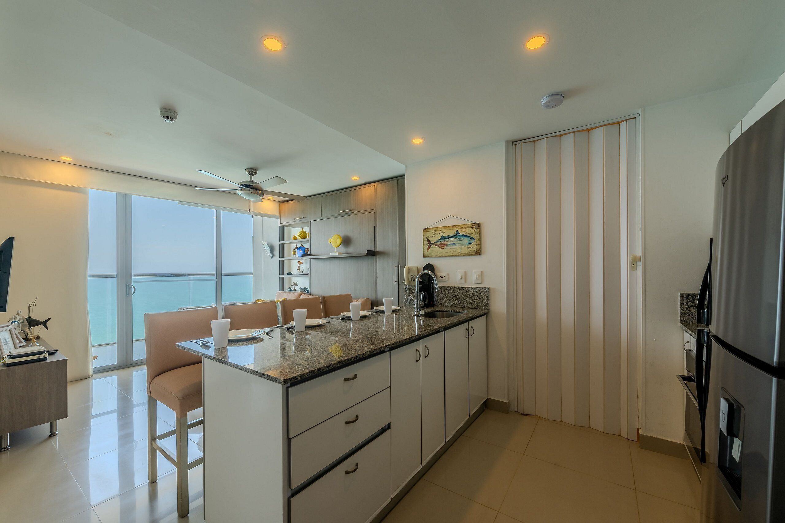 A modern kitchen with a central island, a dining area with a sofa, and a view of the outdoors.