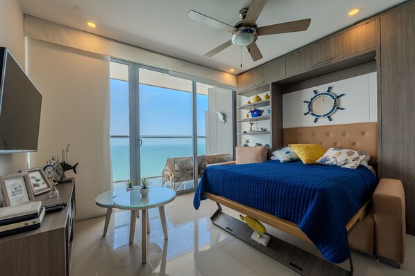 A modern bedroom with a large bed, a ceiling fan, a view of the sea, a small table, and a TV. - 2703 Morros City (Cartagena)